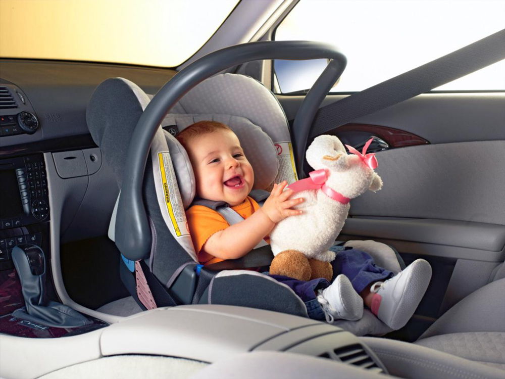 Ребенок с мягкой игрушкой в детском автокресле на переднем сидении
